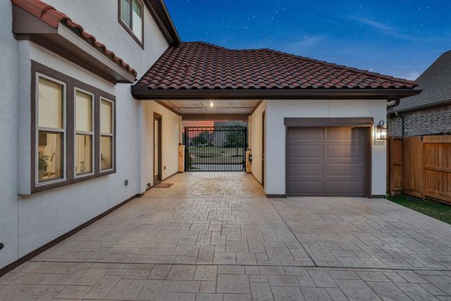 The modern home exterior with a covered driveway and a single-car garage. The house has a tiled roof and large windows, and there's a gated entrance leading to a backyard. | Image 5