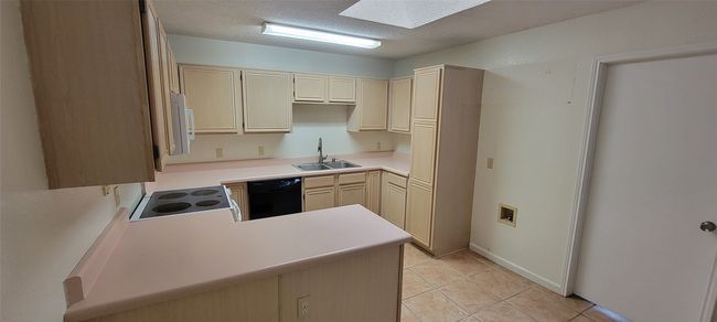 Kitchen with black dishwasher, a sink, stove, light tile patterned flooring, and a textured ceiling | Image 9