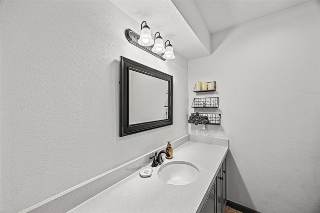 This bathroom features a sleek, modern design with a white countertop and sink, a stylish black framed mirror, and practical shelving for storage. Plenty of space for a vanity area. | Image 18