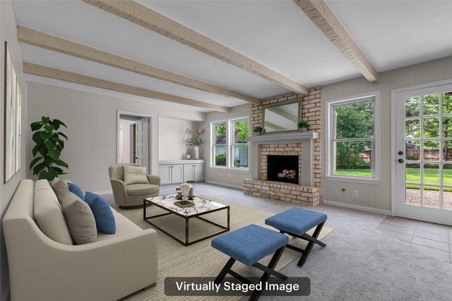 This virtually staged family room features a cozy brick fireplace, exposed ceiling beams, and ample natural light from large windows and a glass door. The neutral color palette and modern furnishings create a welcoming atmosphere. | Image 14