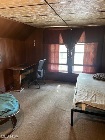 Carpeted bedroom with lofted ceiling and wood walls | Image 2