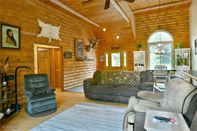 Living room with wood ceiling, a ceiling fan, wood finished floors, a chandelier, and rustic walls | Image 9