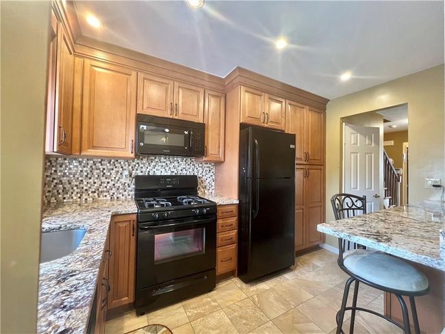 Kitchen with decorative backsplash, sink, light stone counters, black appliances, and a breakfast bar | Image 8