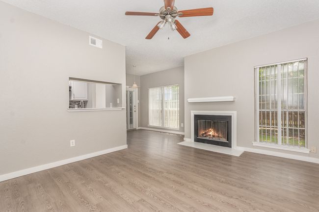 Unfurnished living room with a fireplace with flush hearth, ceiling fan, wood finished floors, baseboards, and a textured ceiling | Image 7