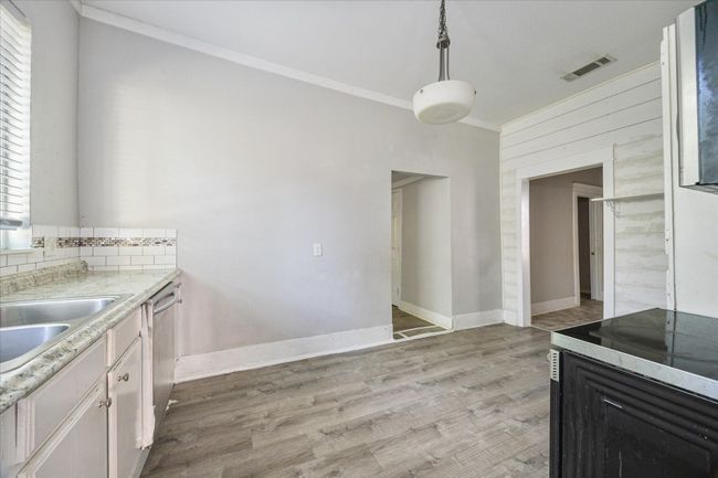 Kitchen featuring light countertops, wooden walls, light wood-style flooring, decorative light fixtures, and ornamental molding | Image 8