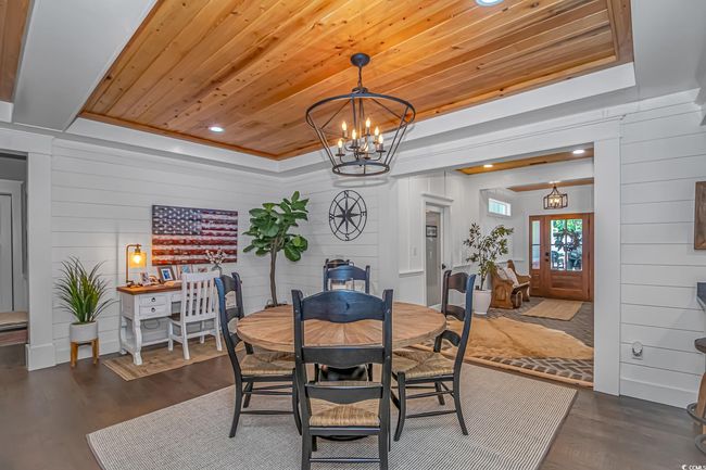 Dining area with a chandelier, dark wood finished floors, wooden ceiling, a raised ceiling, and wood walls | Image 6