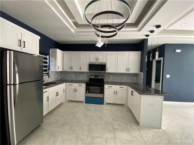 Kitchen with stainless steel appliances, a peninsula, a raised ceiling, light marble finish flooring, and white cabinets | Image 6