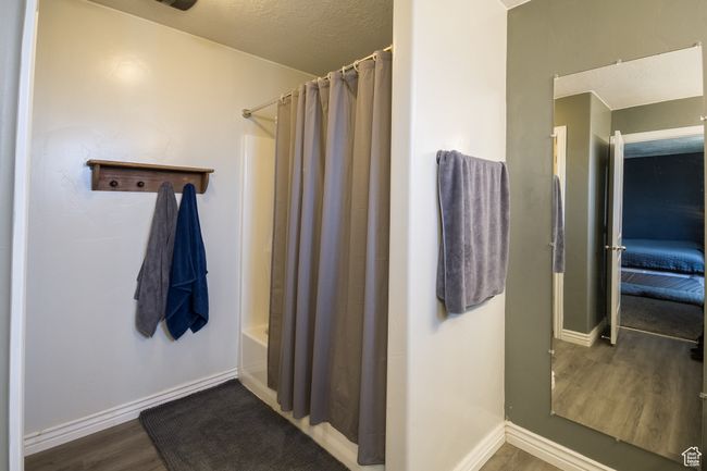 Bathroom with baseboards, shower / tub combo with curtain, wood finished floors, and a textured ceiling | Image 13