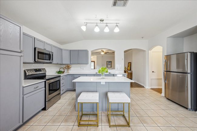 Kitchen with stainless steel appliances, gray cabinets, and light tile patterned floors, and large kitchen island, track lighting and ceiling fan, light countertops, and decorative backsplash | Image 12