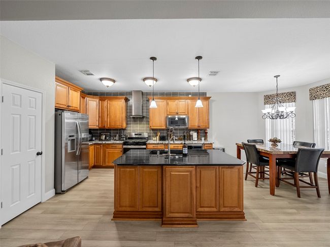 Kitchen with visible vents, wall chimney range hood, a sink, light wood-style floors, and appliances with stainless steel finishes | Image 16