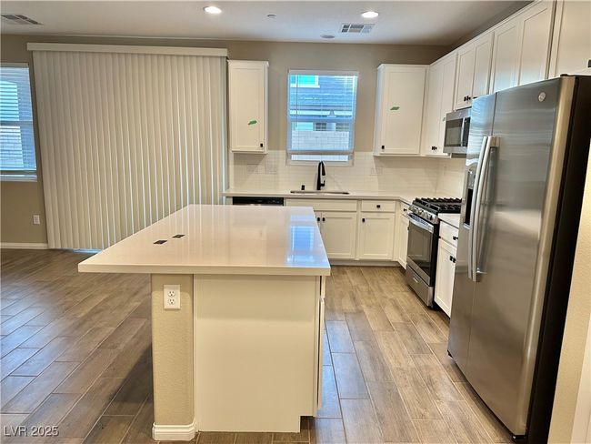 Kitchen featuring visible vents, decorative backsplash, appliances with stainless steel finishes, wood tiled floor, and a sink | Image 17