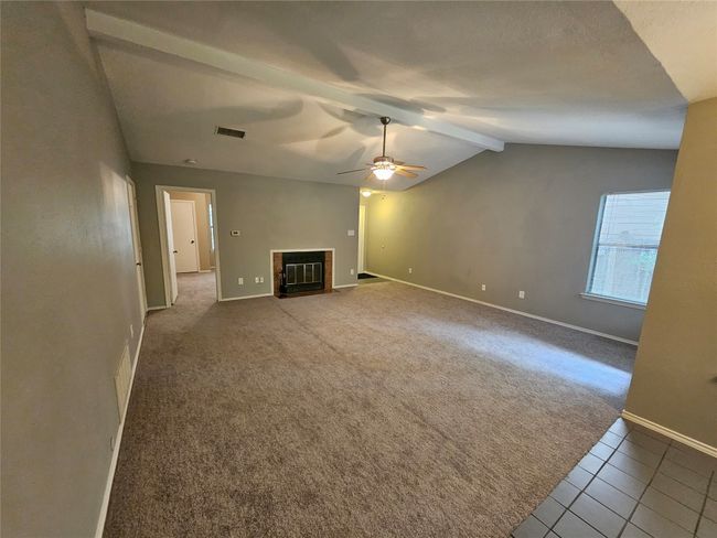 Unfurnished living room with carpet flooring, lofted ceiling with beams, a fireplace with flush hearth, visible vents, and baseboards | Image 6