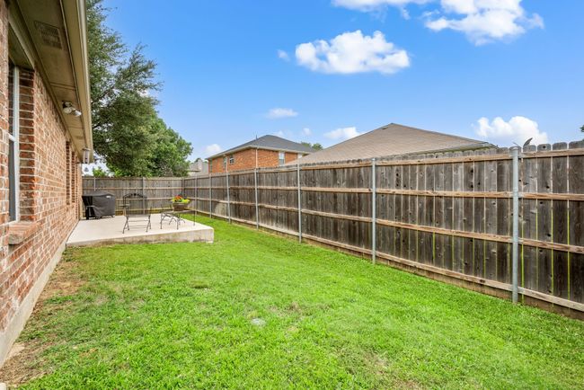 Fenced-in yard with lush grass and full view of the brick rear exterior and patio space. | Image 34