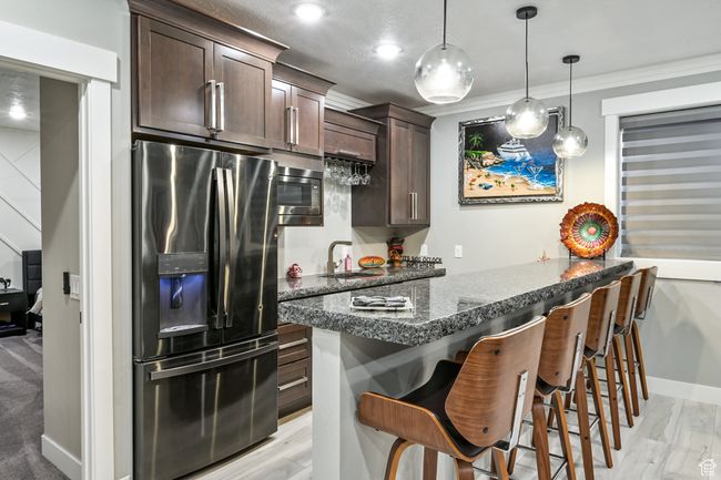 Kitchen with appliances with stainless steel finishes, dark brown cabinetry, a breakfast bar area, light wood finished floors, and hanging light fixtures | Image 67