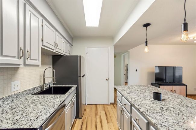 Kitchen featuring stainless steel appliances, light wood finished floors, decorative backsplash, light stone countertops, and pendant lighting | Image 12