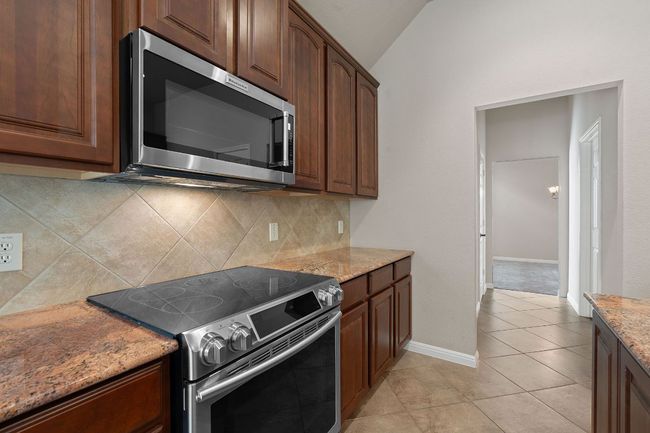 Kitchen featuring stainless steel appliances, granite counters, vaulted ceiling, backsplash, and tile flooring | Image 6