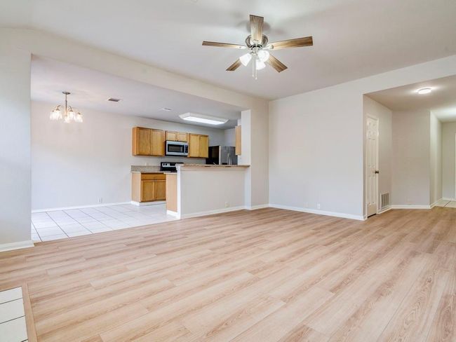 Unfurnished living room featuring light wood-style flooring, ceiling fan, and a chandelier | Image 11