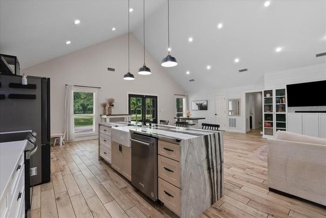 Chef's kitchen with waterfall island, farmhouse sink, pendant lighting, and open flow to dining and living areas. | Image 5