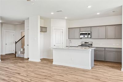 Kitchen featuring backsplash, light hardwood / wood-style flooring, an island with sink, stainless steel appliances, and gray cabinets | Image 3