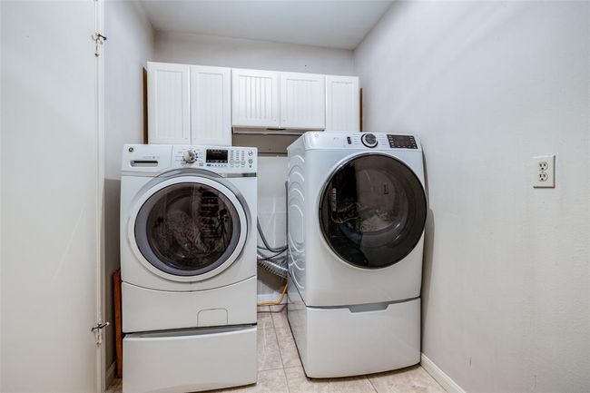 This photo shows a large laundry room with front-loading washer & dryer, white cabinetry above for storage, and a neutral color palette. | Image 19