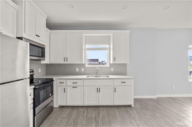 Kitchen featuring appliances with stainless steel finishes, a sink, light countertops, tasteful backsplash, and white cabinetry | Image 11