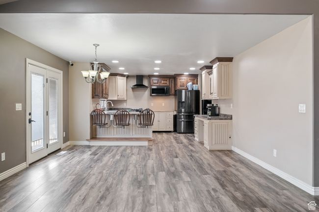 Kitchen with an inviting chandelier, wall chimney exhaust hood, light wood-style flooring, baseboards, and appliances with stainless steel finishes | Image 8