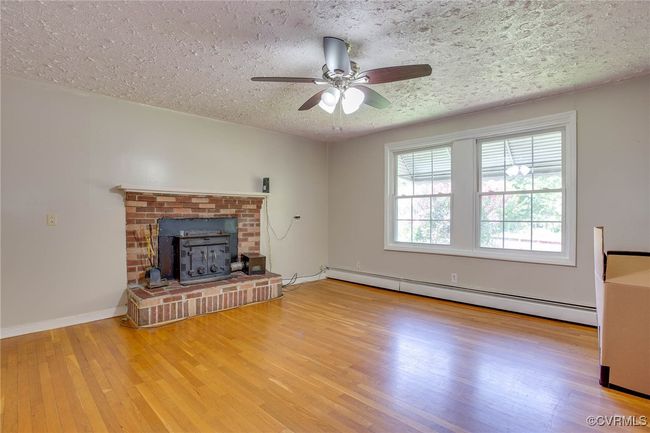Unfurnished living room with light wood-type flooring, a textured ceiling, a brick fireplace, and a baseboard radiator | Image 8