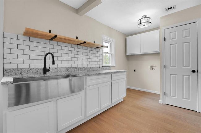 Kitchen with white cabinets, decorative backsplash, light stone counters, and light wood-type flooring | Image 41