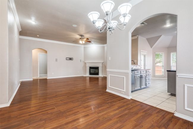 Unfurnished living room featuring arched walkways, a ceiling fan, wood finished floors, a glass covered fireplace, and ornamental molding | Image 9