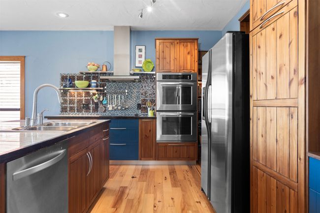 Kitchen featuring ventilation hood, appliances with stainless steel finishes, tasteful backsplash, light wood-type flooring, and sink | Image 13
