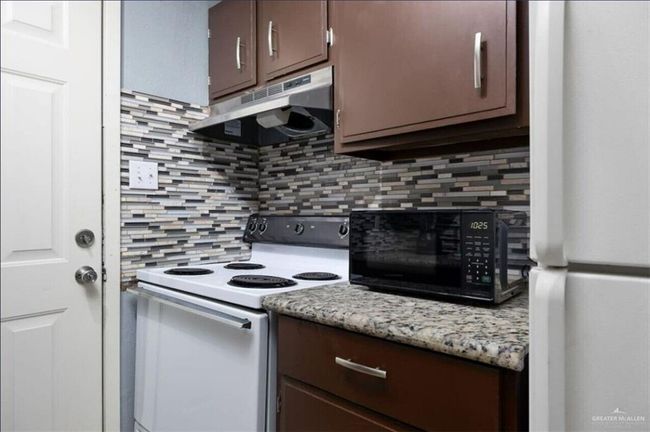 Kitchen featuring under cabinet range hood, white appliances, tasteful backsplash, and dark brown cabinets | Image 5