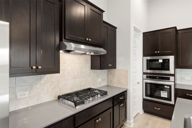 Kitchen with stainless steel appliances, dark brown cabinets, decorative backsplash, and under cabinet range hood | Image 22