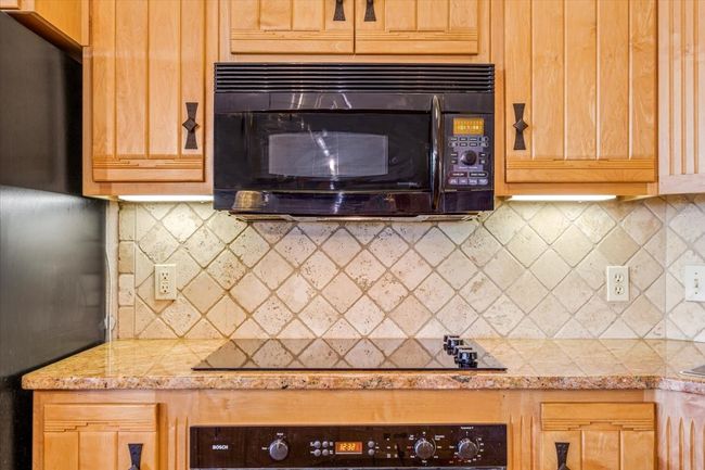 Kitchen with black appliances, decorative backsplash, and light stone counters | Image 15