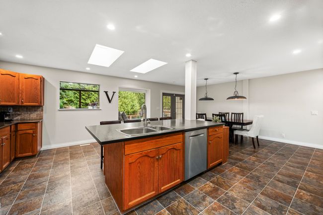 Kitchen featuring tasteful backsplash, dishwasher, a sink, dark countertops, and a skylight | Image 12