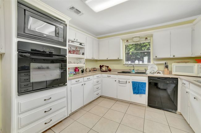 Kitchen with black appliances, a sink, light tile patterned flooring, light countertops, and crown molding | Image 15