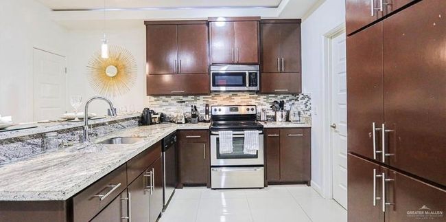 Kitchen featuring backsplash, sink, hanging light fixtures, light tile patterned flooring, and stainless steel appliances | Image 6