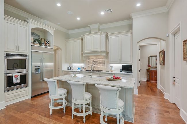 Kitchen featuring stainless steel appliances, open shelves, arched walkways, a kitchen island with sink, and light stone countertops | Image 18