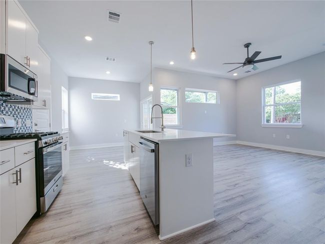 Kitchen featuring stainless steel appliances, a center island with sink, light wood-style flooring, ceiling fan, and recessed lighting | Image 12