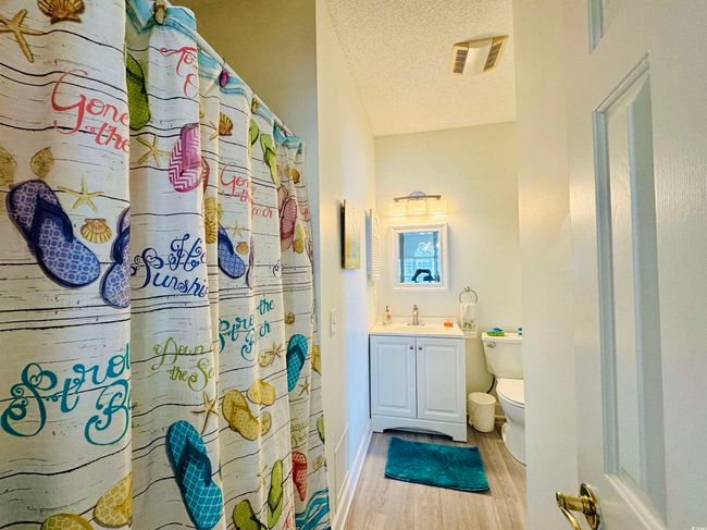 Bathroom featuring wood finished floors, a textured ceiling, toilet, vanity, and curtained shower | Image 16