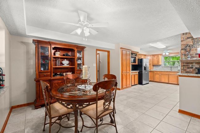 This photo showcases a spacious kitchen and dining area with tiled flooring. The kitchen features wooden cabinets, a modern refrigerator, and ample counter space. | Image 8