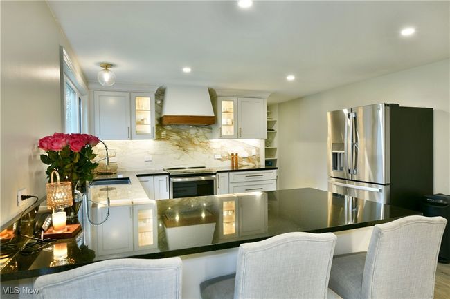 Kitchen featuring white cabinets, appliances with stainless steel finishes, a peninsula, custom range hood, and decorative backsplash | Image 13