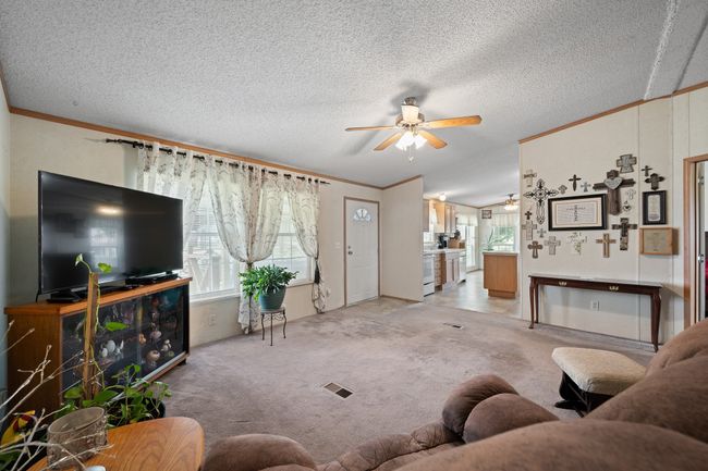 Living room with a ceiling fan, ornamental molding, light carpet, opens into the kitchen and dining area | Image 8
