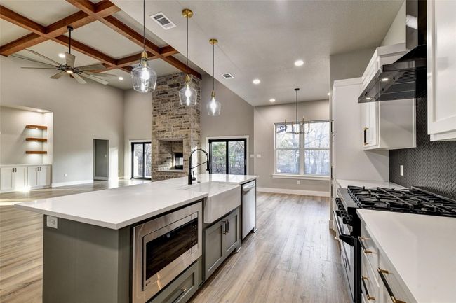 Kitchen featuring coffered ceiling, white cabinets, a spacious island, wall chimney range hood, and appliances with stainless steel finishes | Image 20