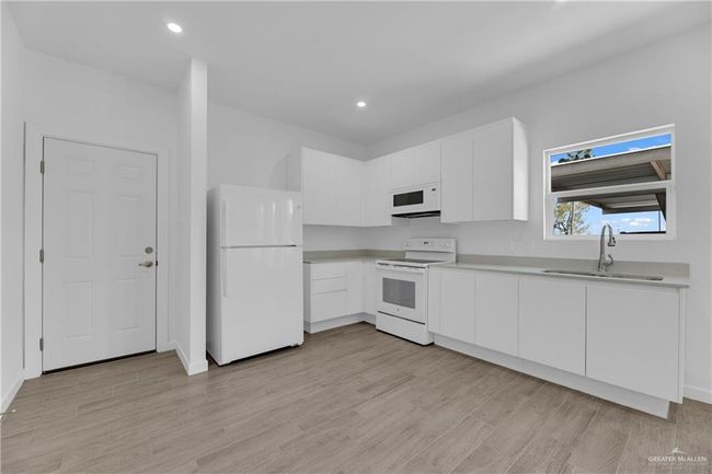 Kitchen featuring white cabinetry, sink, white appliances, and light wood-type flooring | Image 6