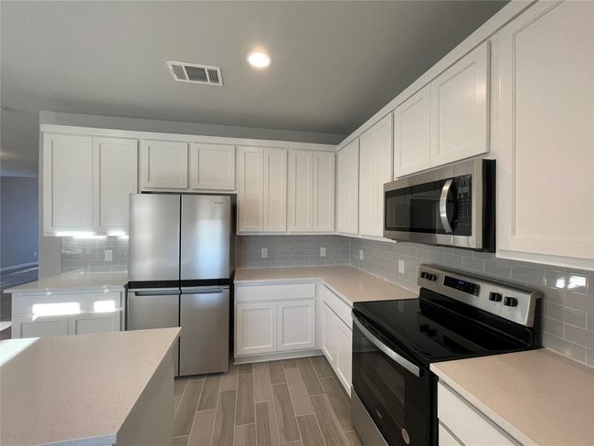 Kitchen featuring appliances with stainless steel finishes, white cabinets, decorative backsplash, light wood-style floors, and recessed lighting | Image 7