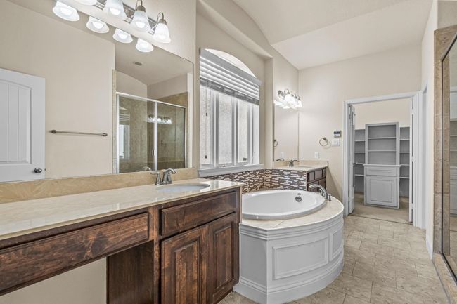 Bathroom featuring a stall shower, a spacious closet, two vanities, a bath, and vaulted ceiling | Image 18