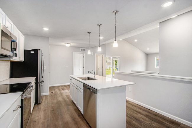 Bright, white kitchen cabinetry is accented by white quartz counters and tile backsplash. The kitchen island provides prep and sitting space and is accented by pendant lighting above. Stainless steel appliances are included! | Image 6