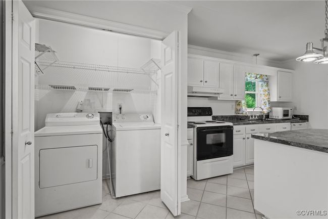 Kitchen with white cabinets, range with electric cooktop, under cabinet range hood, white microwave, and washer and dryer | Image 12