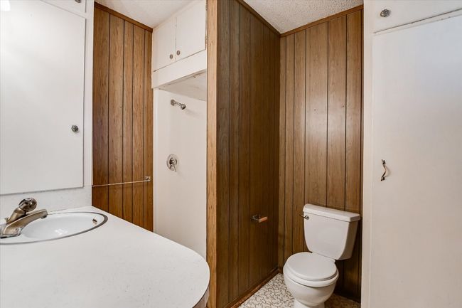 Bathroom with toilet, a textured ceiling, wooden walls, and a sink | Image 9