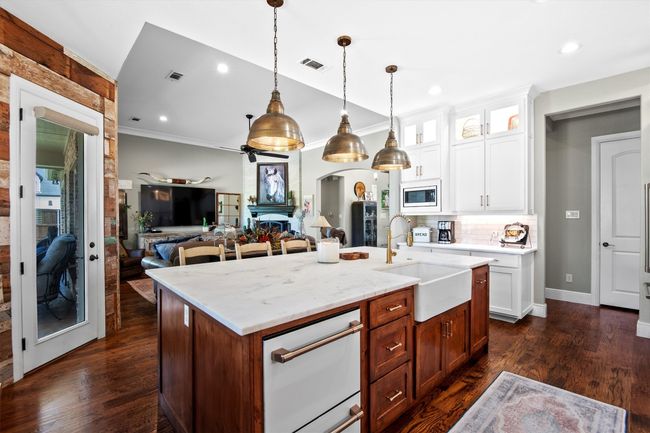 Kitchen with stainless steel microwave, open floor plan, a center island with sink, glass insert cabinets, and white dishwasher | Image 12